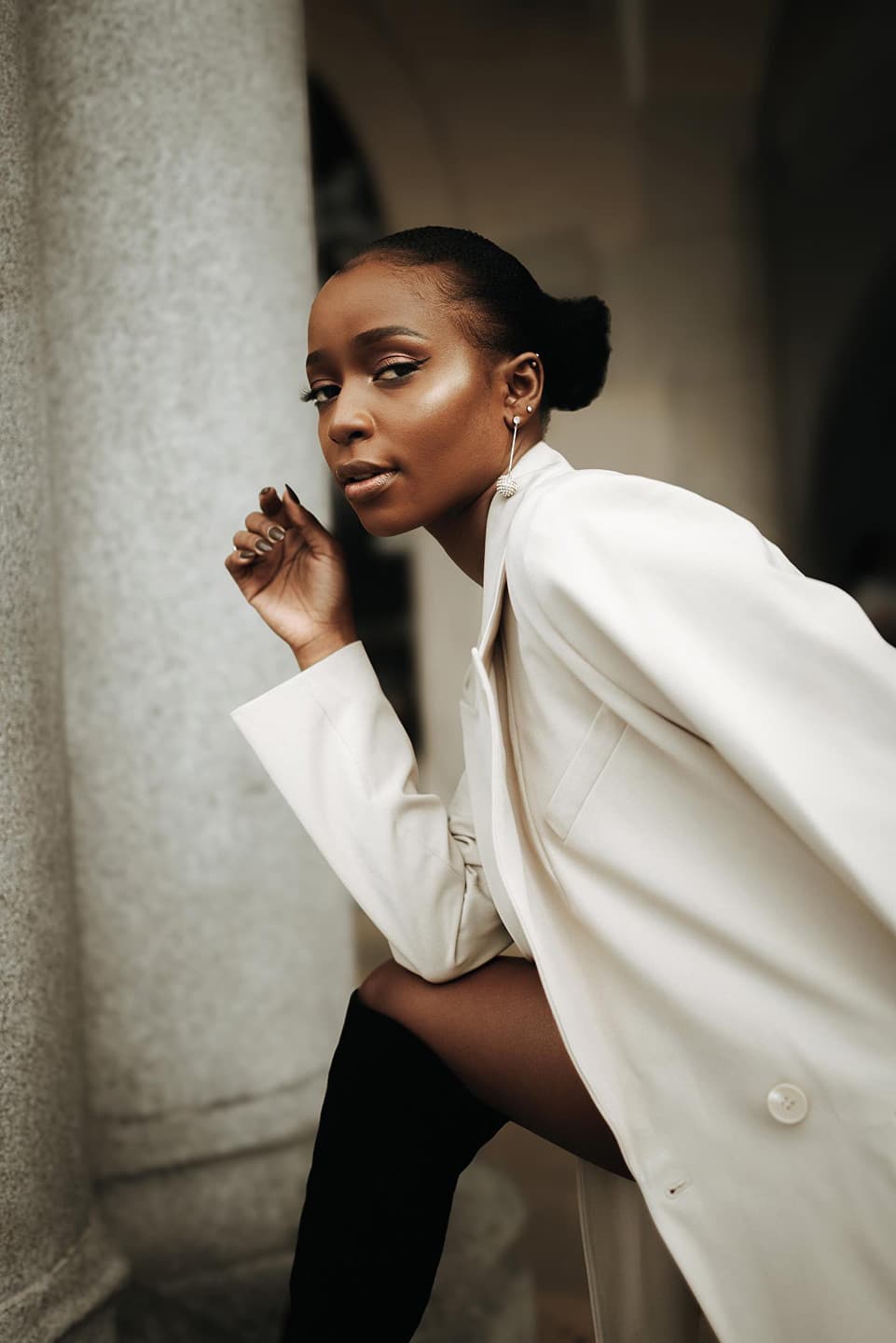 Black and white portrait of Becky Sangolo in an oversized cream blazer leaning against a stone column